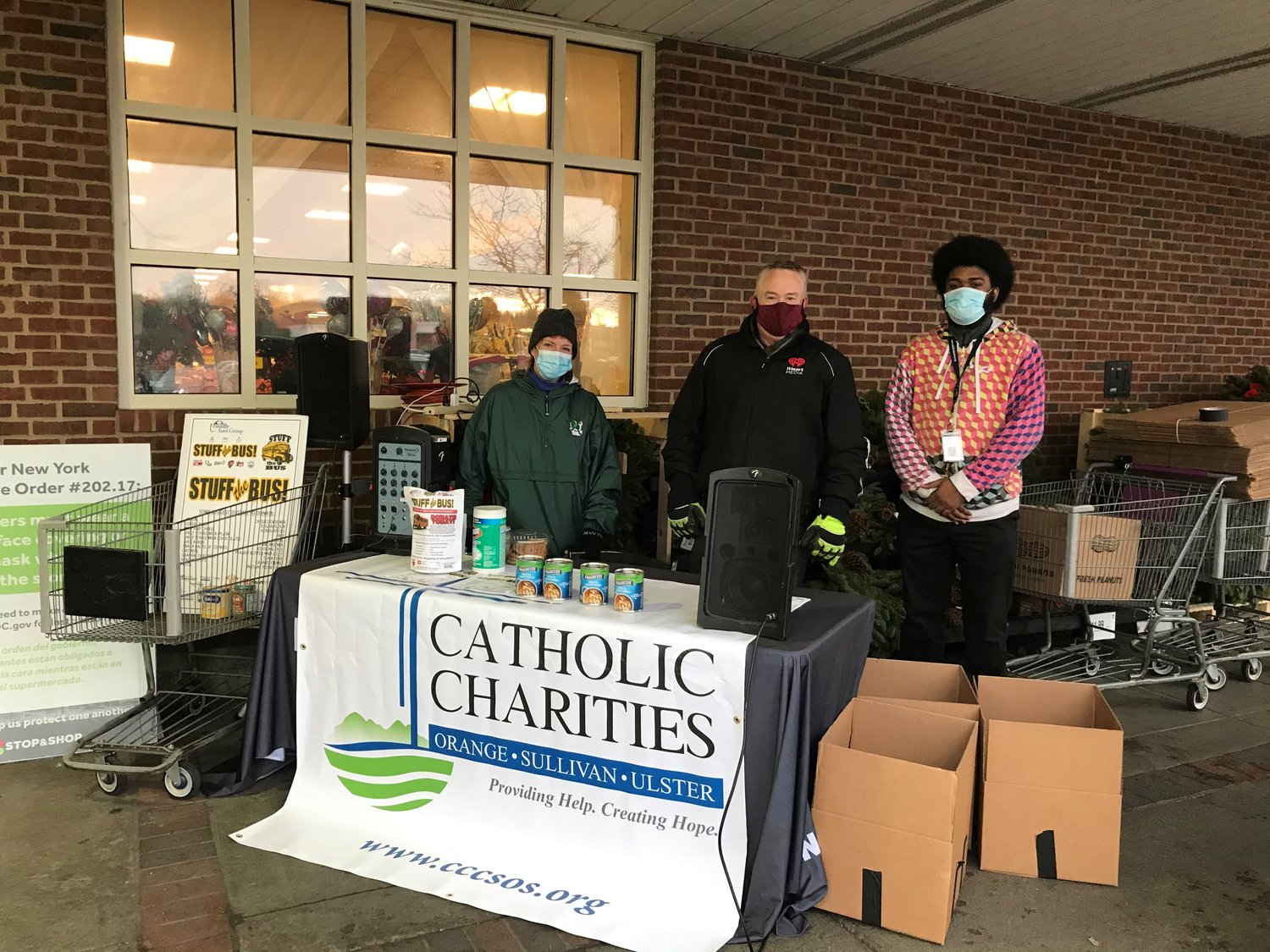 Catholic Charities’ team members Kathy Beckvermit, left, and Glenn Granum, right are joined by iHeartMedia Senior Vice President of Sales Rob VanDerbeck, center, at the 23rd annual Friendly Auto Group Stuff-the-Bus food drive.